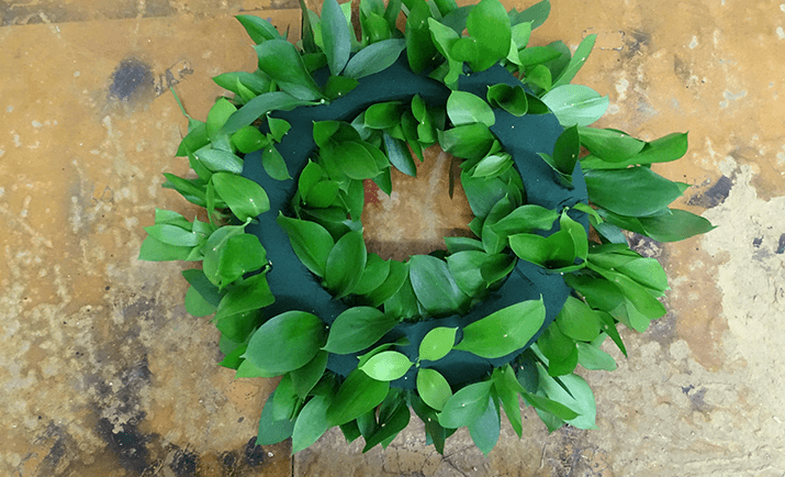 Continue to fill in the base with your chosen foliage. Here, we are only using the Hard Ruscus as the foliage, but you can use other types i.e Eucalyptus, Salal, Dusty Miller etc. for added texture and interest.