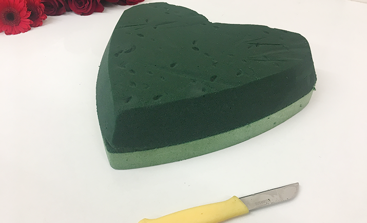 Gather your florist tools, including 12" floral foam heart (open or solid), a pair of scissors and a florist knife. Soak the floral foam in water for a few minutes. Round the edges of your floral foam heart. This is to help with a shaping of your floral wreath.